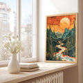Framed artwork of a mountain landscape with a sunset on a windowsill  A desert landscape with cacti and a winding river Desert Canyon Wall Art, Sunset Landscape Poster, placed on a wooden floor.