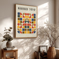 Framed Bauhaus 1919 poster on a wall with decorative plants and books.