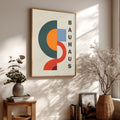 Bauhaus style poster on a wall with decorative plants and books below.
