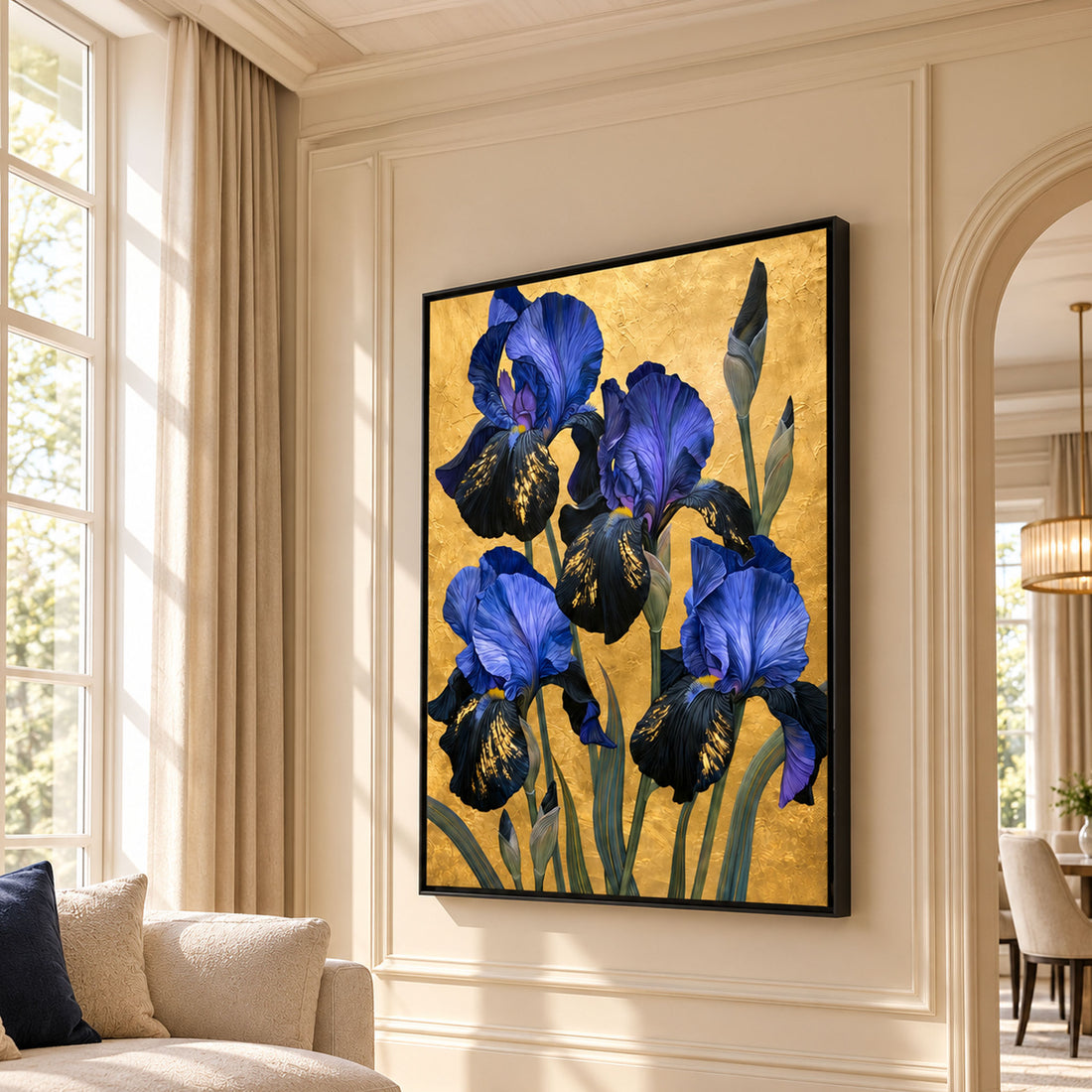 A framed canvas wall art print featuring blue irises on a textured gold background, displayed in a real living room setting with beige walls, a window, curtains, and a sofa.
