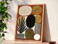 Mid century modern boho abstract art print featuring a geometric arrangement of organic shapes on a terracotta rust background. Graphic elements include a black palm plant in a striped pot, a gold leopard print oval, metallic gold circles, a black and white striped rectangle, and an off-white oval with concentric gold rings.