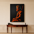 A framed vertical canvas print of a stylized portrait of Lord Hanuman in profile, rendered in vivid orange and red tones against a black background. The frame hangs on a beige wall above a dark wood console table with decorative objects.