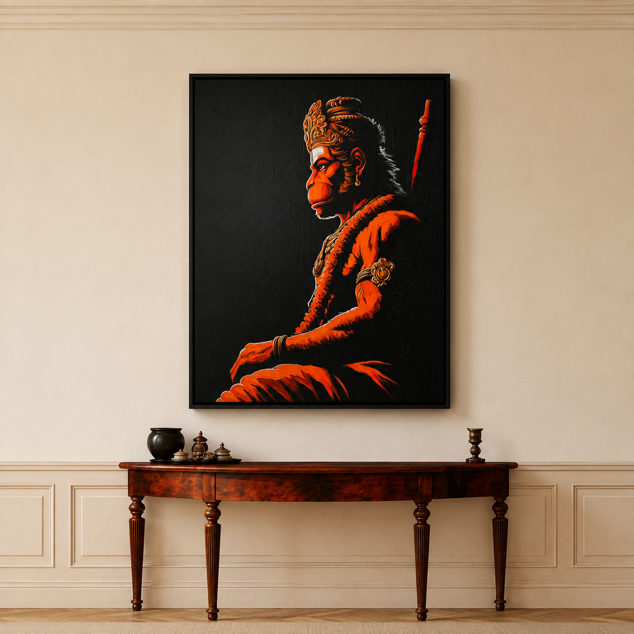 A framed vertical canvas print of a stylized portrait of Lord Hanuman in profile, rendered in vivid orange and red tones against a black background. The frame hangs on a beige wall above a dark wood console table with decorative objects.