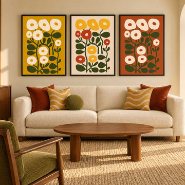  mid-century modern floral art prints in yellow, red, and orange tones are displayed above a cream-colored sofa with decorative throw pillows in a warm, sunlit living room.
